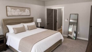 A bedroom with a bed, nightstands, a lamp, a mirror, and a door. - The Rock House | Walk to OSU (Stillwater)