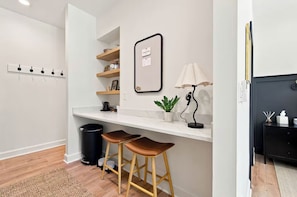 A modern kitchen with a white countertop, two stools, a black trash bin, and a wall-mounted mirror.