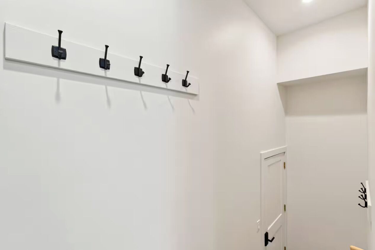 Un couloir avec un mur blanc, une porte dotée d’une poignée noire et une étagère blanche avec des crochets noirs.