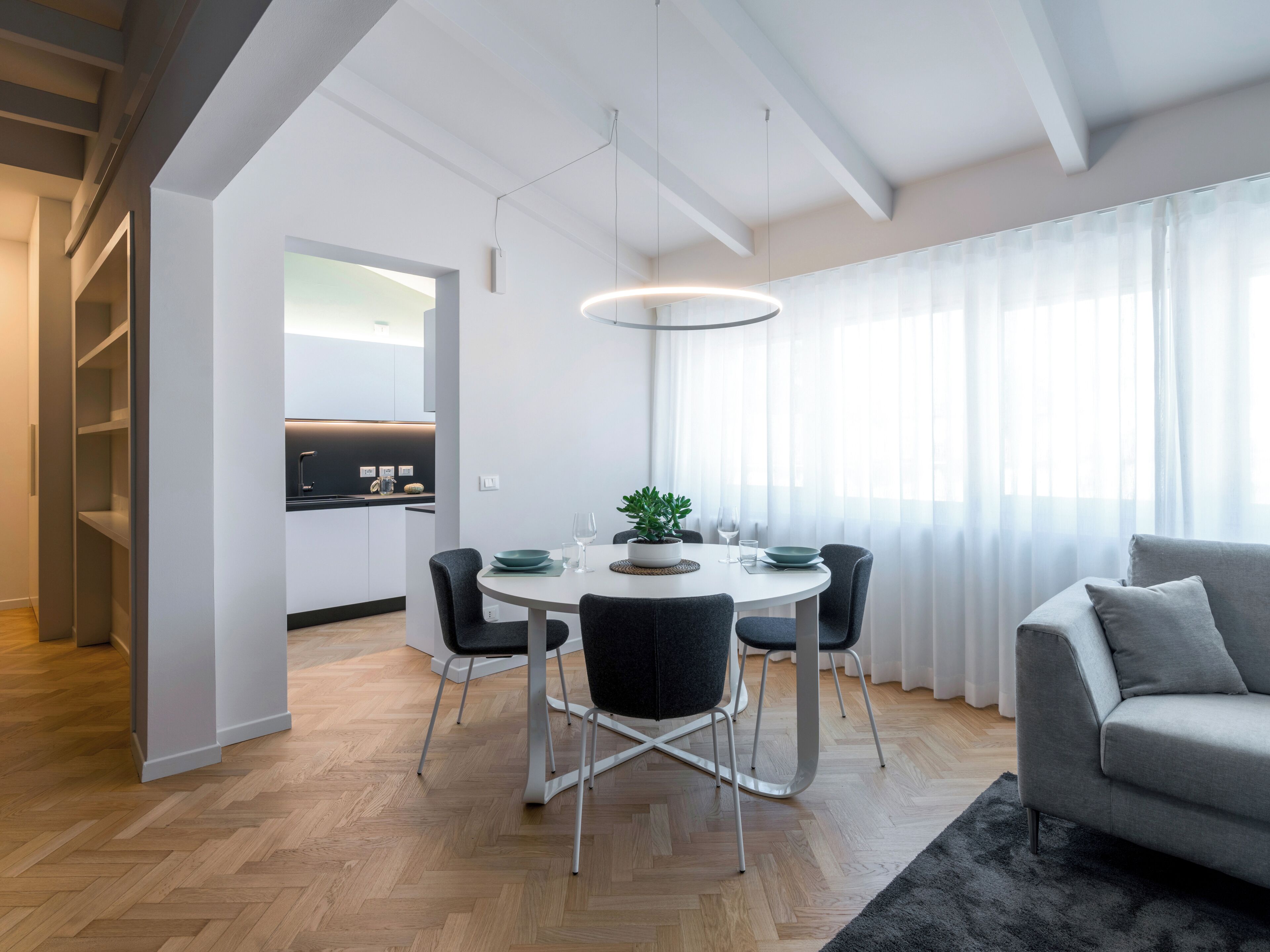 A modern living space with a dining area, a sofa, and a kitchen in the background.