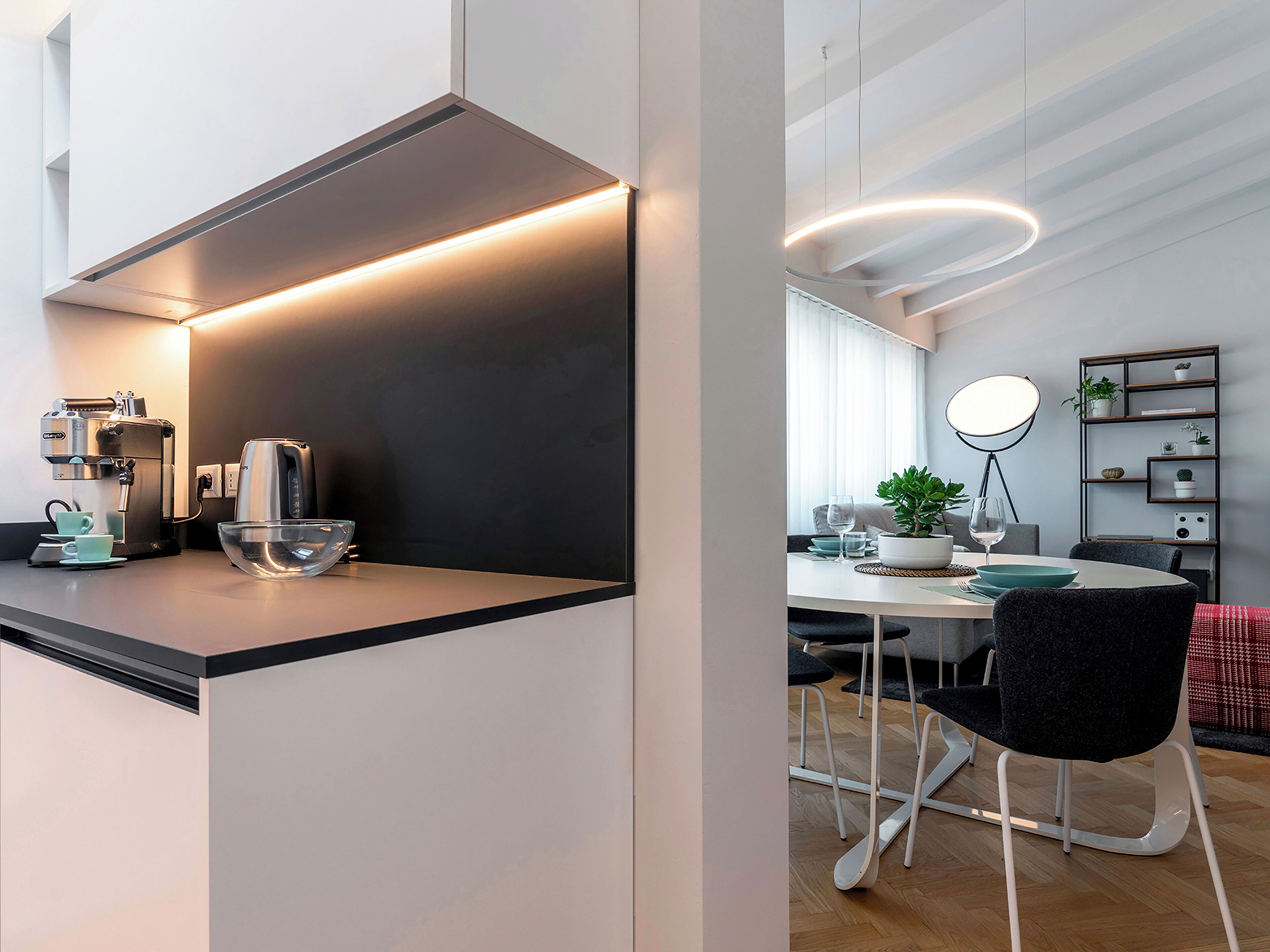 Una cucina moderna con una macchina da caffè, una ciotola e un'area pranzo con tavolo, sedie e una pianta.