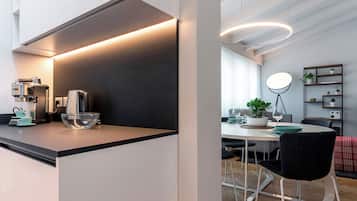Una cucina moderna con una macchina da caffè, una ciotola e un'area pranzo con tavolo, sedie e una pianta.