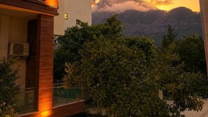Um edifício moderno de dois andares com varanda, piscina e vista para montanhas ao pôr do sol.