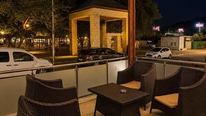 Uma área de estar externa com móveis de vime, um gazebo e vista para a rua à noite.