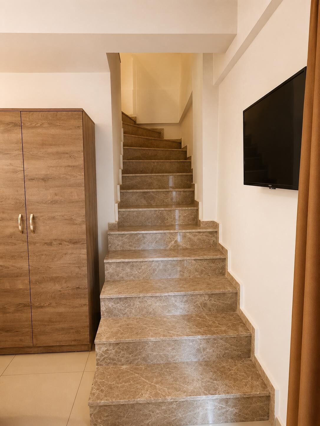 A staircase with a wooden wardrobe and a flat-screen TV on the wall.