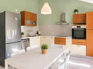 Eine moderne Küche mit Edelstahl-Kühlschrank, Holzschränken, einem eingebauten Backofen und einem Esstisch mit Stühlen.