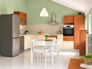 Eine moderne Küche mit einem Edelstahl-Kühlschrank, Holzschränken, einem weißen Esstisch mit Stühlen und einer hängenden Pendelleuchte.