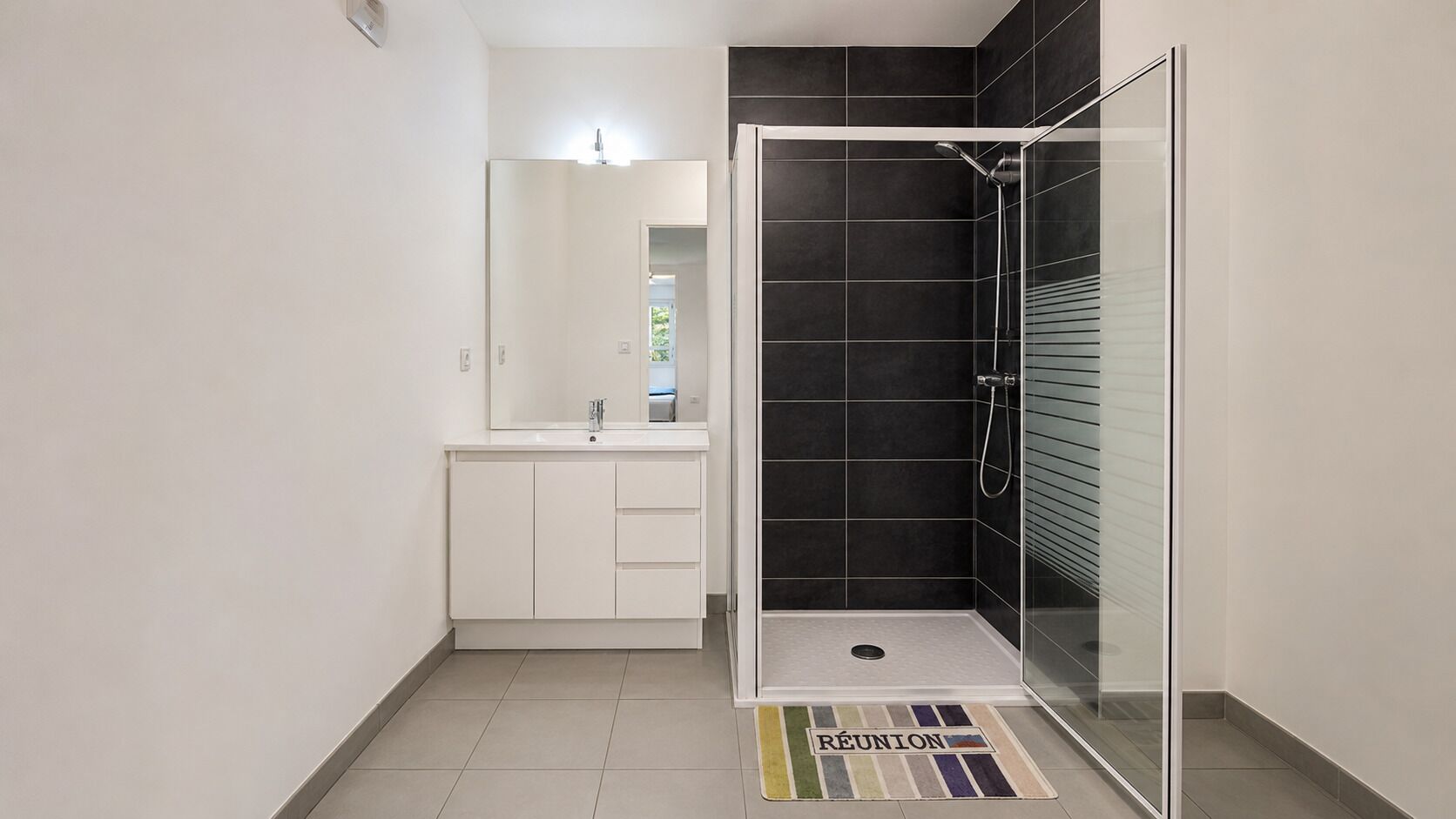 Une salle de bain moderne avec une douche à parois de verre, un meuble-lavabo blanc avec un miroir et un sol carrelé.