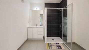 Une salle de bain moderne avec une douche à parois de verre, un meuble-lavabo blanc avec un miroir et un sol carrelé.