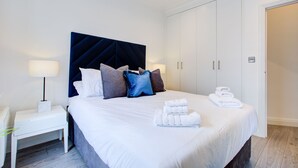 A hotel room with a large bed, a bedside table with a lamp, a wardrobe, and a door. - Hybrid Resi - Fulham - Three-Bedroom Apartment (London)
