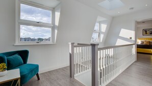 A spacious room with a large window, a teal chair, and a white railing. - Hybrid Resi - Fulham - Three-Bedroom Apartment (London)