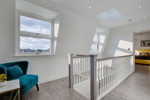 Ein geräumiges Zimmer mit großem Fenster, einem türkisfarbenen Sessel und einer weißen Geländer.
