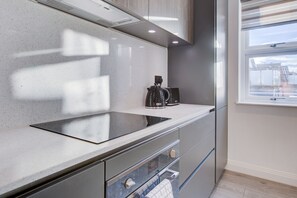 A modern kitchen with a sleek countertop, a built-in oven, and a window with a view of the outside. - Hybrid Resi - Fulham - Three-Bedroom Apartment (London)