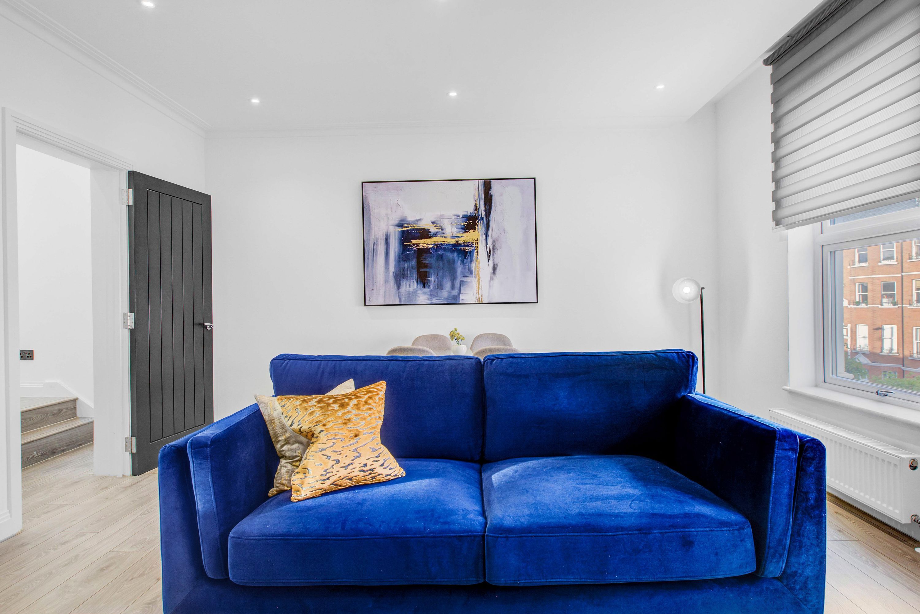 Un salon moderne avec un canapé bleu, un tableau accroché au mur et une fenêtre avec des stores.