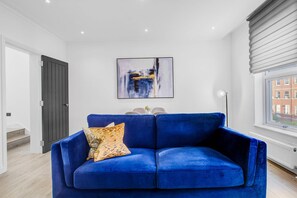 Un salon moderne avec un canapé bleu, un tableau accroché au mur et une fenêtre avec des stores.