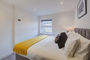 Une chambre à coucher avec un lit, une fenêtre, une table de chevet avec une lampe et un tableau accroché au mur.