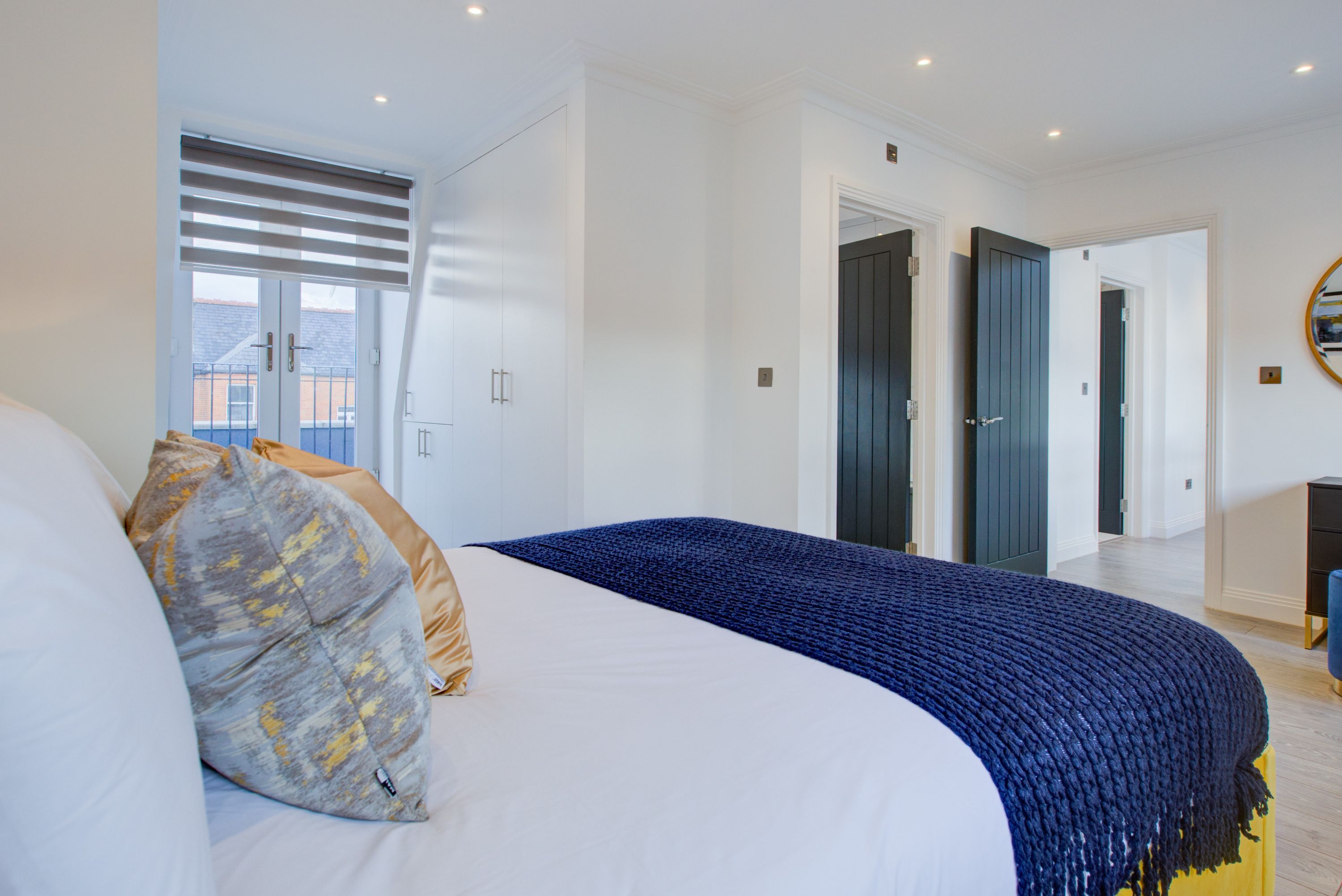 Ein modernes Schlafzimmer mit einem großen Bett, einem Fenster mit Jalousien und einer Tür zu einem anderen Raum.