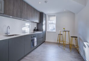 Une cuisine moderne avec des meubles gris, un évier en acier inoxydable et une fenêtre équipée de stores.