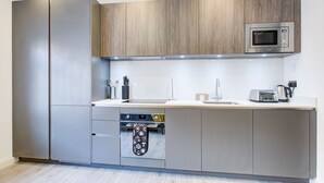 A modern kitchen with stainless steel appliances, wooden cabinets, and a built-in oven. - Hybrid Resi - Fulham - Three-Bedroom Apartment (London)