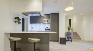 A modern kitchen with a central island, bar stools, a microwave, and a staircase leading to another level. - Hybrid Resi - Fulham - Two-Bedroom Apartment (London)