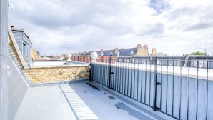 Eine Dachterrasse mit Steinmauer, Metallgeländer und Blick auf Wohnhäuser.