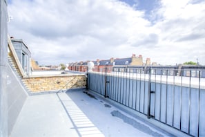 En takterrass med en mur av sten, ett metallräcke och utsikt över bostadshus.