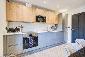 A modern kitchen with wooden cabinets, a Bosch microwave, a built-in oven, and a sink. - Hybrid Resi - Fulham - Two-Bedroom Apartment (London)