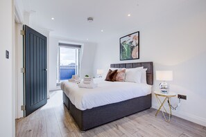 Quarto moderno com uma cama grande, uma mesa de cabeceira com abajur e vista para a cidade pela janela.