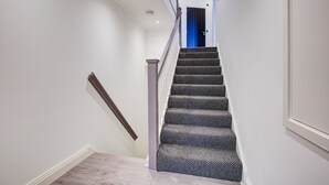 Eine Treppe mit einem gemusterten Teppich, weißen Wänden und einer blauen Tür am oberen Ende.