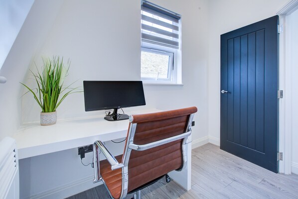 A modern office space with a white desk, a computer monitor, a brown leather chair, a potted plant, and a dark blue door.