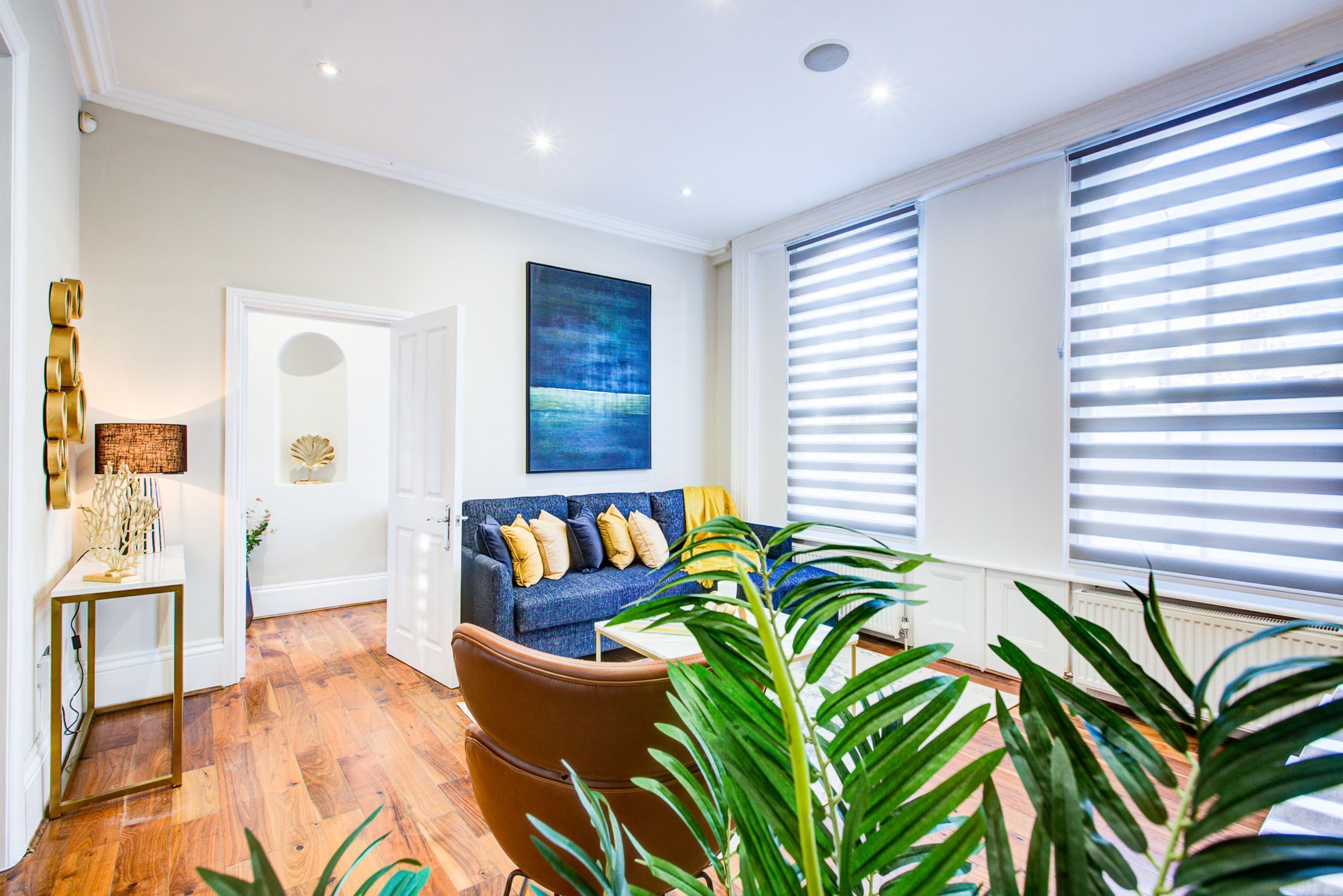 A modern living room with a blue sofa, a brown armchair, and a large window with blinds.
