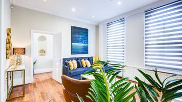 A modern living room with a blue sofa, a brown armchair, and a large window with blinds.