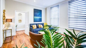 Una sala de estar moderna con un sofá azul, una mesa de centro de madera y un gran ventanal con persianas.