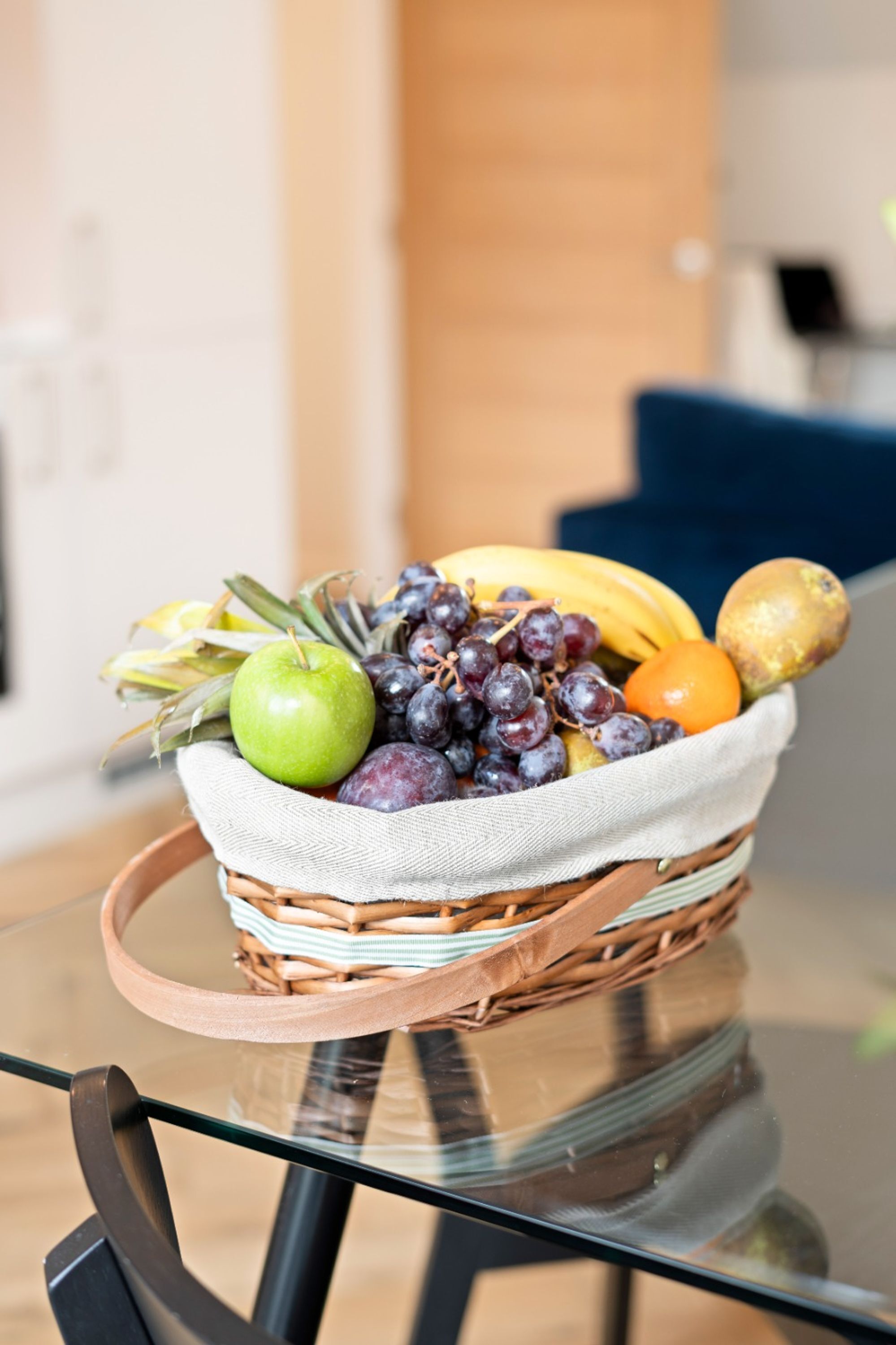 A wicker fruit basket on a glass table with a chair beside it.