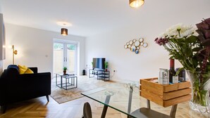 Un salon moderne avec une table basse en verre, un canapé noir et un coin repas agrémenté d’un buffet en bois.