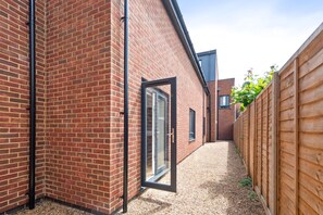 A narrow alleyway with a brick building, a wooden fence, and a clear sky.