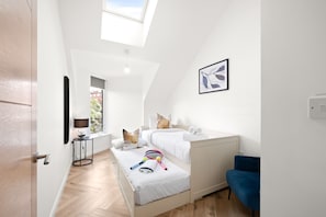Un dormitorio con techo inclinado, una cama, una mesita de noche con lámpara, una ventana y un interruptor de luz en la pared.