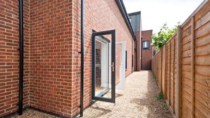 A narrow alleyway with a brick building, a wooden fence, and a door leading to a covered area. - Hybrid Resi - Mitcham - Two-Bedroom Apartment (Mitcham)