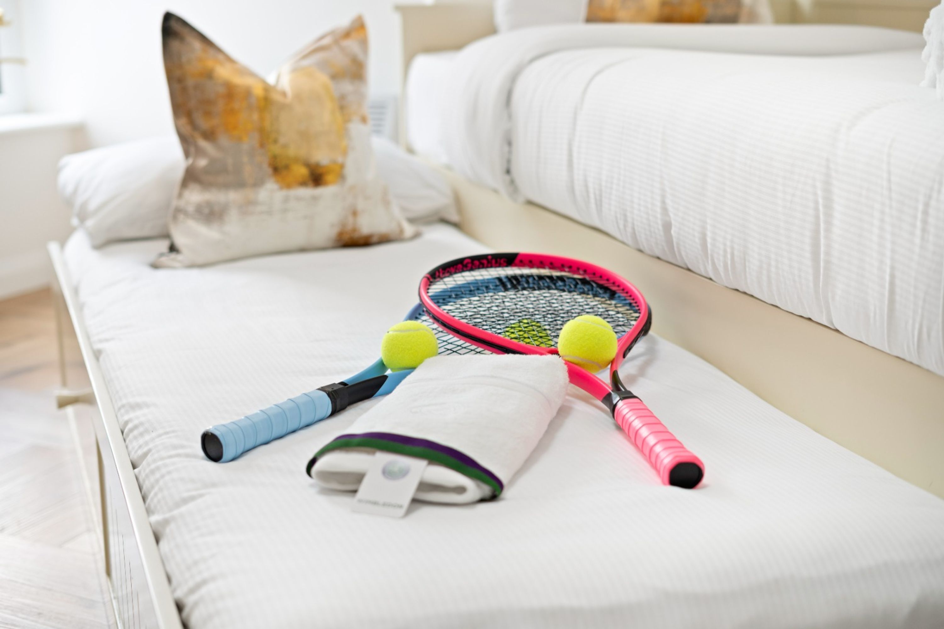 A neatly made bed with pillows, a tennis racket, and two tennis balls.