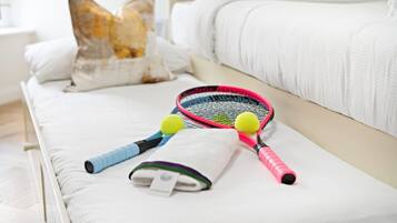 A neatly made bed with pillows, a tennis racket, and two tennis balls.