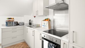A modern kitchen with white cabinets, a built-in oven, a stovetop, and a microwave. - Hybrid Resi - Mitcham - Two-Bedroom Apartment (Mitcham)