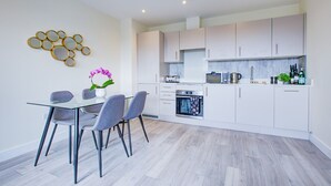 Une cuisine moderne avec des armoires blanches, un four encastré et un coin repas comprenant une table et des chaises en verre.