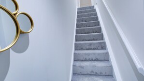 Una escalera con revestimiento de alfombra y una pared blanca con un espejo circular dorado.