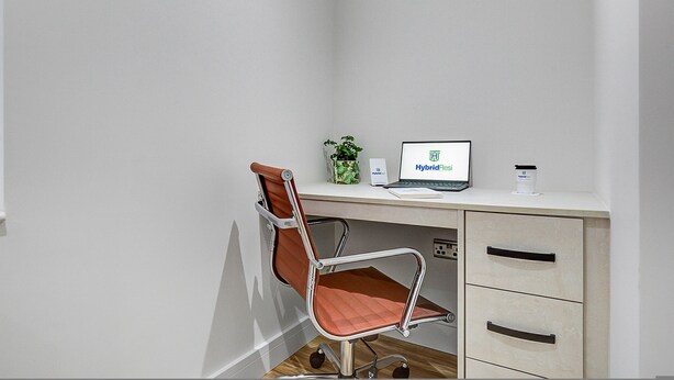 Oficina en esquina con escritorio, silla, laptop, planta en maceta y un mueble bajo.