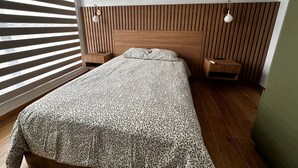 Una habitación de hotel con cama, mesita de noche, lámpara, ventana con persianas y unidad de aire acondicionado.