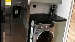 Una cocina compacta con refrigerador, lavadora y cafetera.