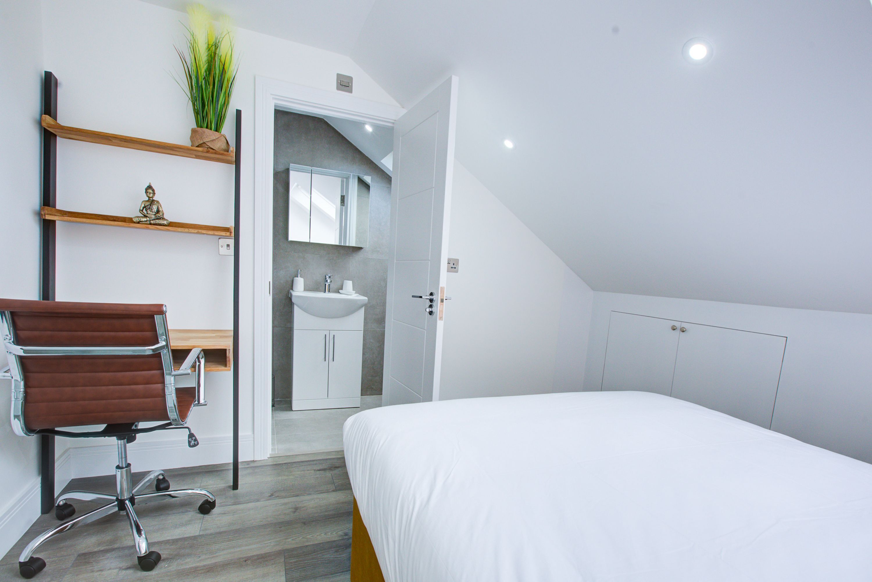 Een moderne slaapkamer met een bed, een bureau met stoel, een badkamer met wastafel en een kledingkast.