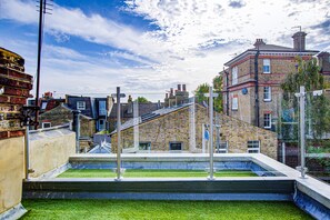 A rooftop terrace with a small grassy area, a metal railing, and a view of surrounding buildings. - Hybrid Resi - Wandsworth - Apartment (London)