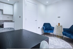A modern living room with a dark wooden table, two blue armchairs, a small round table with a golden base, and a white door. - Hybrid Resi - Wandsworth - Apartment (London)