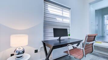 A modern office space with a desk, computer, chair, lamp, and a window with blinds.
